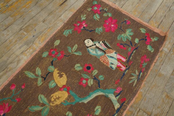 Brown embroidered rug featuring a stylized person, magenta flowers, and green leaves on rustic wooden floorboards.