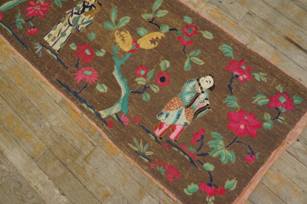 Colorful figural and floral embroidered runner with a brown field resting on distressed wood planks.