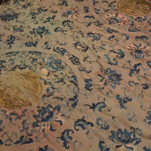 A light tan textile features a dense blue floral scroll pattern and distinct gold circular motifs.