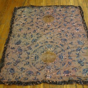 A thin, embroidered textile with blue floral vines and gold medallions rests on worn wood planks.