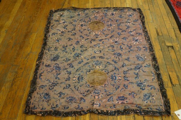 A thin, embroidered textile with blue floral vines and gold medallions rests on worn wood planks.