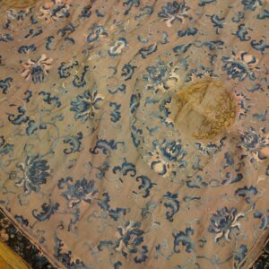 Flat textile with blue and pink floral embroidery and metallic gold accents covers a wood floor.
