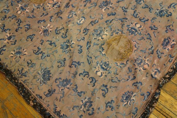 Flat textile with blue and pink floral embroidery and metallic gold accents covers a wood floor.
