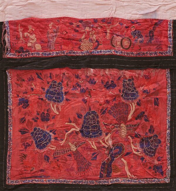 Red embroidered textile featuring blue floral designs, stylized birds, and figural scenes, framed by black borders.