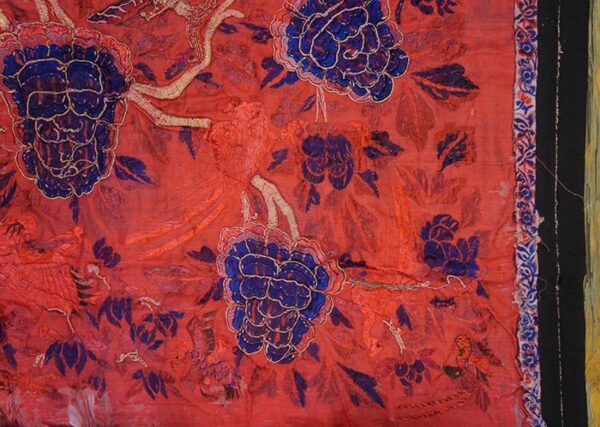 Highly textured red textile fragment featuring large blue flowers and intricate gold embroidered details.