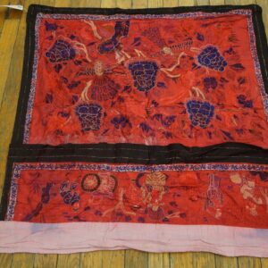 Red embroidered textile with purple florals and black borders lies on distressed wooden flooring.