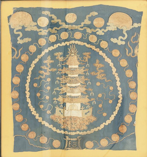 Framed blue textile featuring a central pagoda design, gold coiled circles, and stylized cloud patterns.