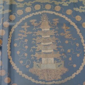 Framed blue textile with embroidered tan pagoda, cloud shapes, and spiraled medallion patterns.
