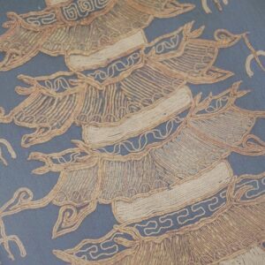 Close-up of blue fabric with highly textured, raised tan corded patterns and geometric designs.