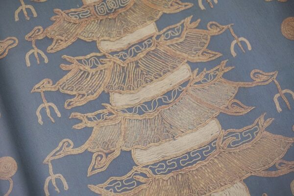 Close-up of blue fabric with highly textured, raised tan corded patterns and geometric designs.