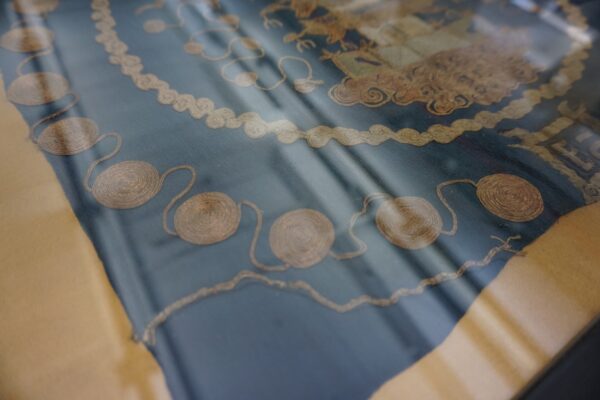 Detailed view of a low-pile navy textile featuring thick, coiled gold cord applique designs.