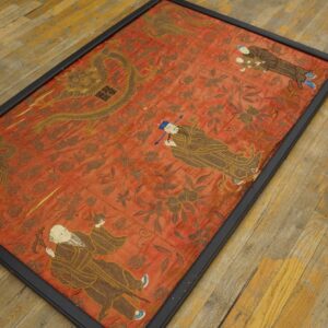 Framed reddish textile featuring gold dragons, phoenix, and figures lies on weathered wood floor.