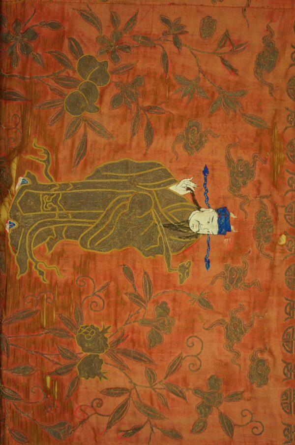 Low-pile rust textile with gold and brown embroidery showing a reclining figure and floral motifs.