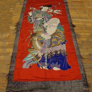 Narrow red runner with detailed figural embroidery on a plank wood floor.