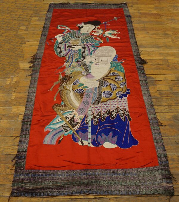 Narrow red runner with detailed figural embroidery on a plank wood floor.