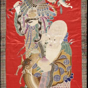 Vertical red textile hanging featuring detailed multicolored embroidery of two figures and a geometric border.