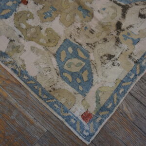 Distressed rug corner with blue border and faded olive designs lies on weathered brown hardwood.