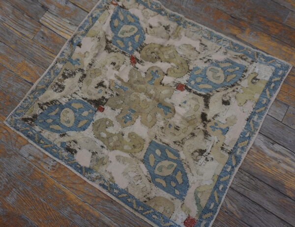Distressed blue, beige, and olive patterned rug lying on rustic gray wooden planks.