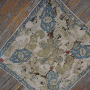 Heavily distressed rug with cream, dusty blue, and sage pattern rests diagonally on worn wooden floorboards.