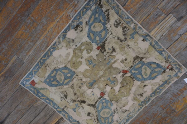 Heavily distressed rug with cream, dusty blue, and sage pattern rests diagonally on worn wooden floorboards.