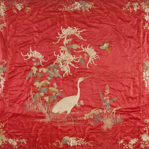 A square, bright red embroidered textile features a white crane, large white flowers, and a small bird within a dense floral border.