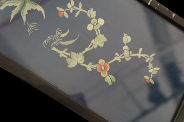 Navy textile with detailed embroidered botanical motifs in pale green and coral, bordered by dark wood.