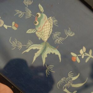 Dark blue embroidered textile featuring a detailed cream and green goldfish and stylized floral branches.