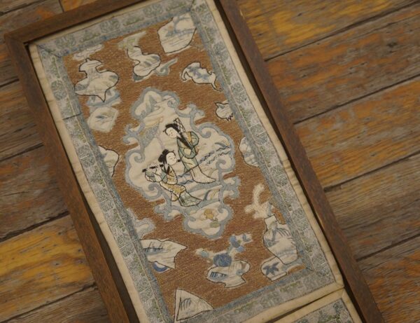 A framed rust and blue flat-weave textile showing two figures, resting on rustic wooden floorboards.