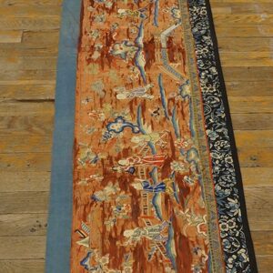 Long, narrow orange and blue textile runner featuring figural patterns, set upon light wood flooring.