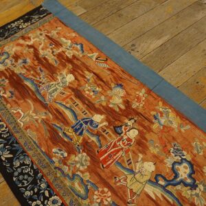 Rust-colored low pile runner with light blue and white figural and floral patterns on a worn hardwood floor.