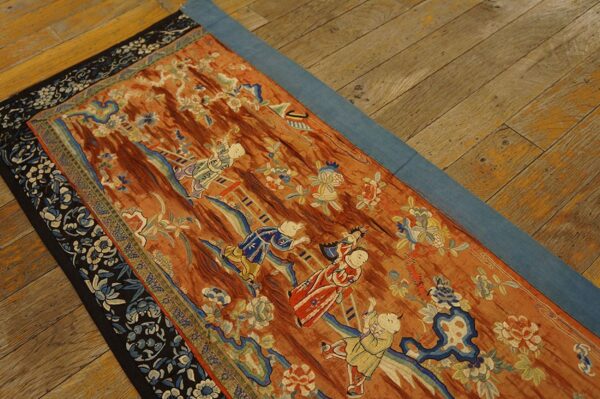 Rust-colored low pile runner with light blue and white figural and floral patterns on a worn hardwood floor.