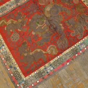 Low pile embroidered red textile featuring mythical brown lions, mirrored borders, and distressed wood flooring.