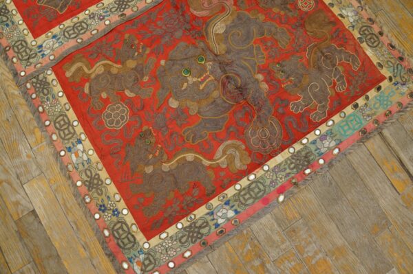 Low pile embroidered red textile featuring mythical brown lions, mirrored borders, and distressed wood flooring.