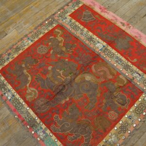 A red embroidered textile featuring brown mythological lions and mirrored borders rests on worn wooden floors.
