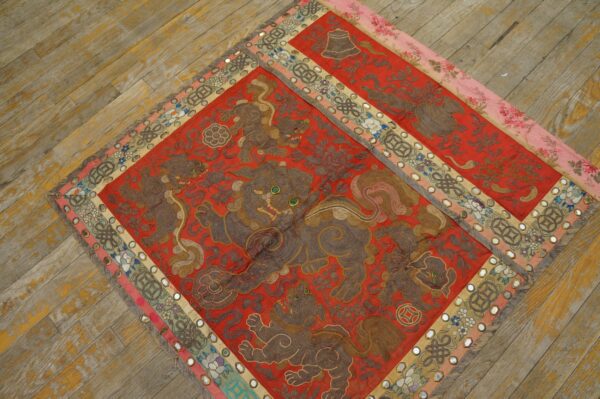A red embroidered textile featuring brown mythological lions and mirrored borders rests on worn wooden floors.