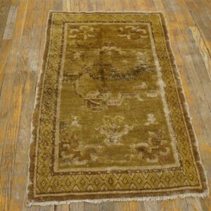 A distressed olive green and brown patterned rug with short fringe rests on aged wooden floorboards.