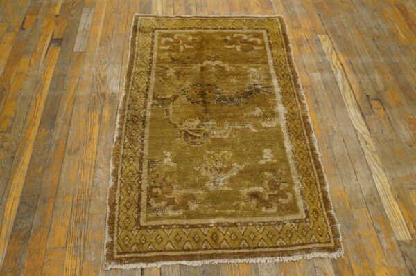 A distressed olive green and brown patterned rug with short fringe rests on aged wooden floorboards.