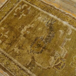 Highly distressed gold and brown area rug runner with a geometric border on wood floors.
