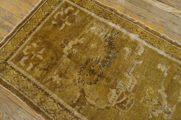Highly distressed gold and brown area rug runner with a geometric border on wood floors.