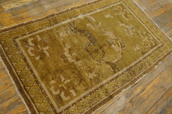 A distressed olive and brown traditional rug with geometric borders sits on rustic wooden floorboards.