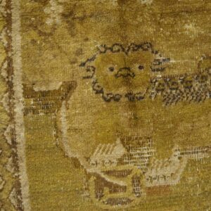A worn mustard yellow rug with a dark, stylized animal motif rests on distressed wooden planks.