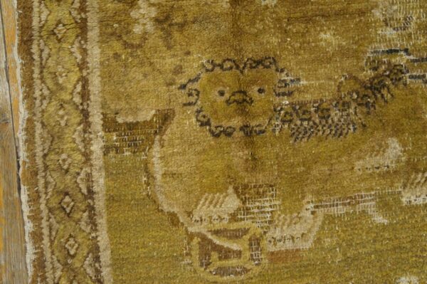 A worn mustard yellow rug with a dark, stylized animal motif rests on distressed wooden planks.