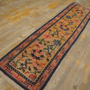 A narrow runner with gold, red, and blue floral patterns and a geometric border on distressed wood.