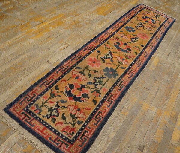 A narrow runner with gold, red, and blue floral patterns and a geometric border on distressed wood.