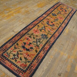 Orange floral runner rug with navy blue and red geometric borders rests on worn wood plank flooring.