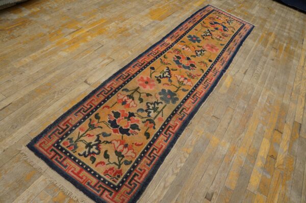 Orange floral runner rug with navy blue and red geometric borders rests on worn wood plank flooring.