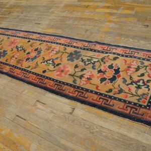 Yellow floral runner rug with blue and red designs and a geometric border on distressed wooden floors.