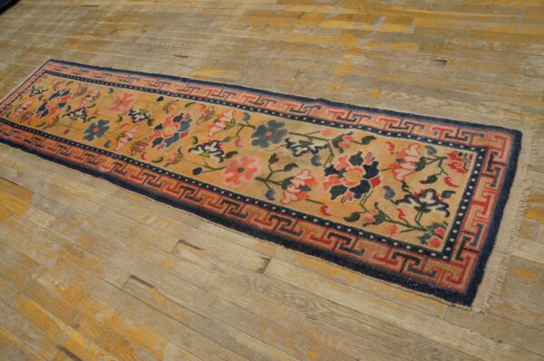 Yellow floral runner rug with blue and red designs and a geometric border on distressed wooden floors.