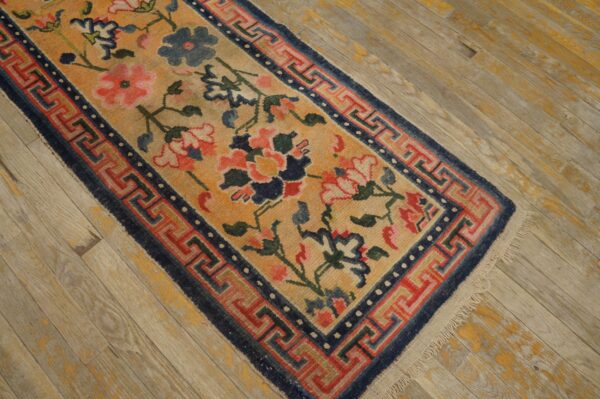 Low-pile floral runner in gold, coral, and navy blue lies diagonally on weathered wood floor.