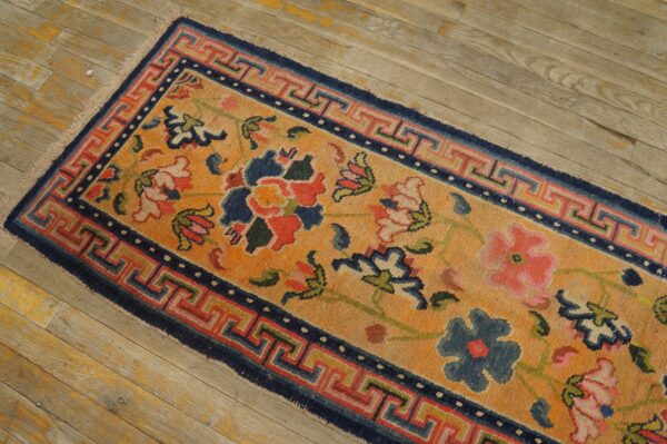 Golden orange runner rug featuring multicolored floral motifs and a detailed geometric border on wood flooring.